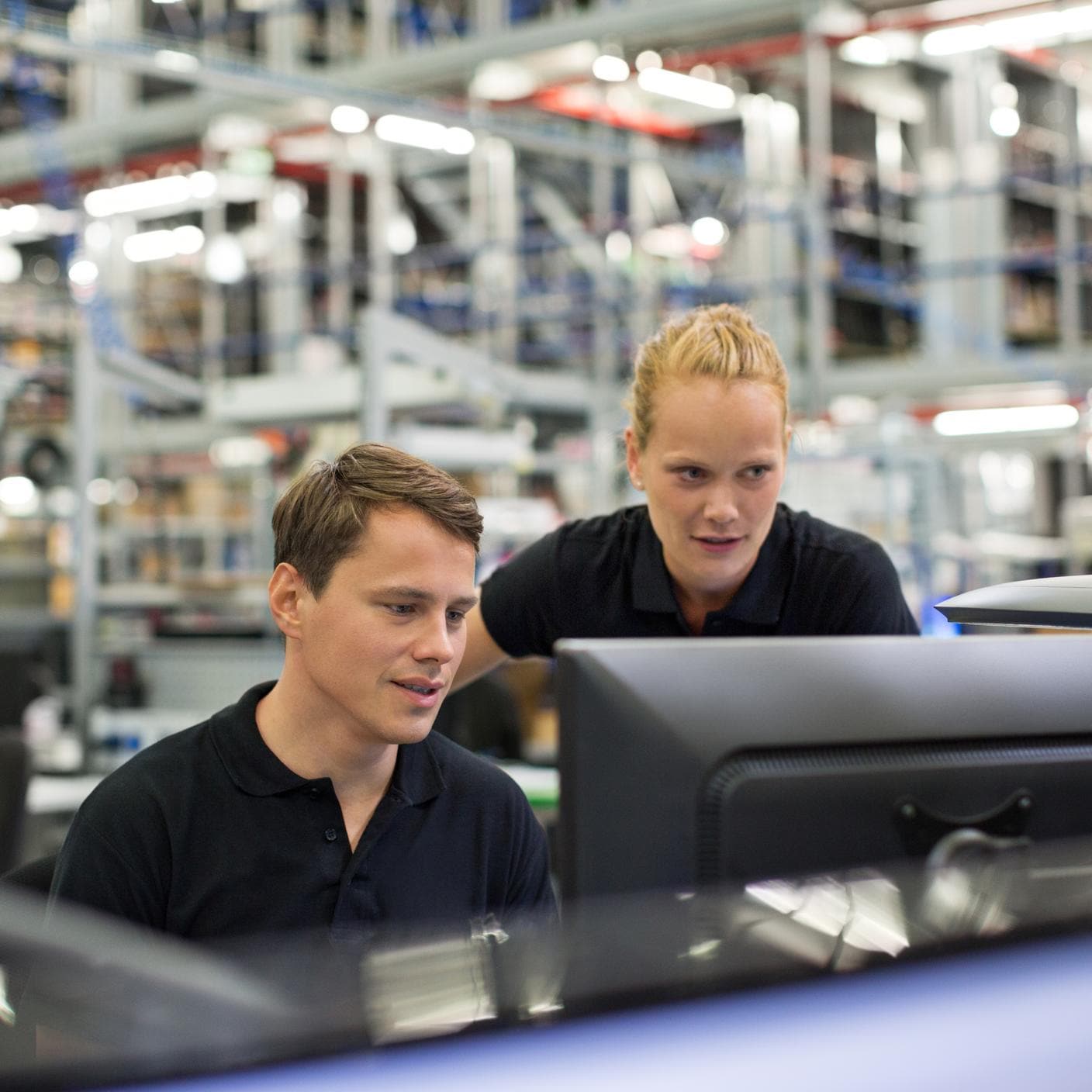 Two people in a warehouse sitting in front of a computer looking at the screen
